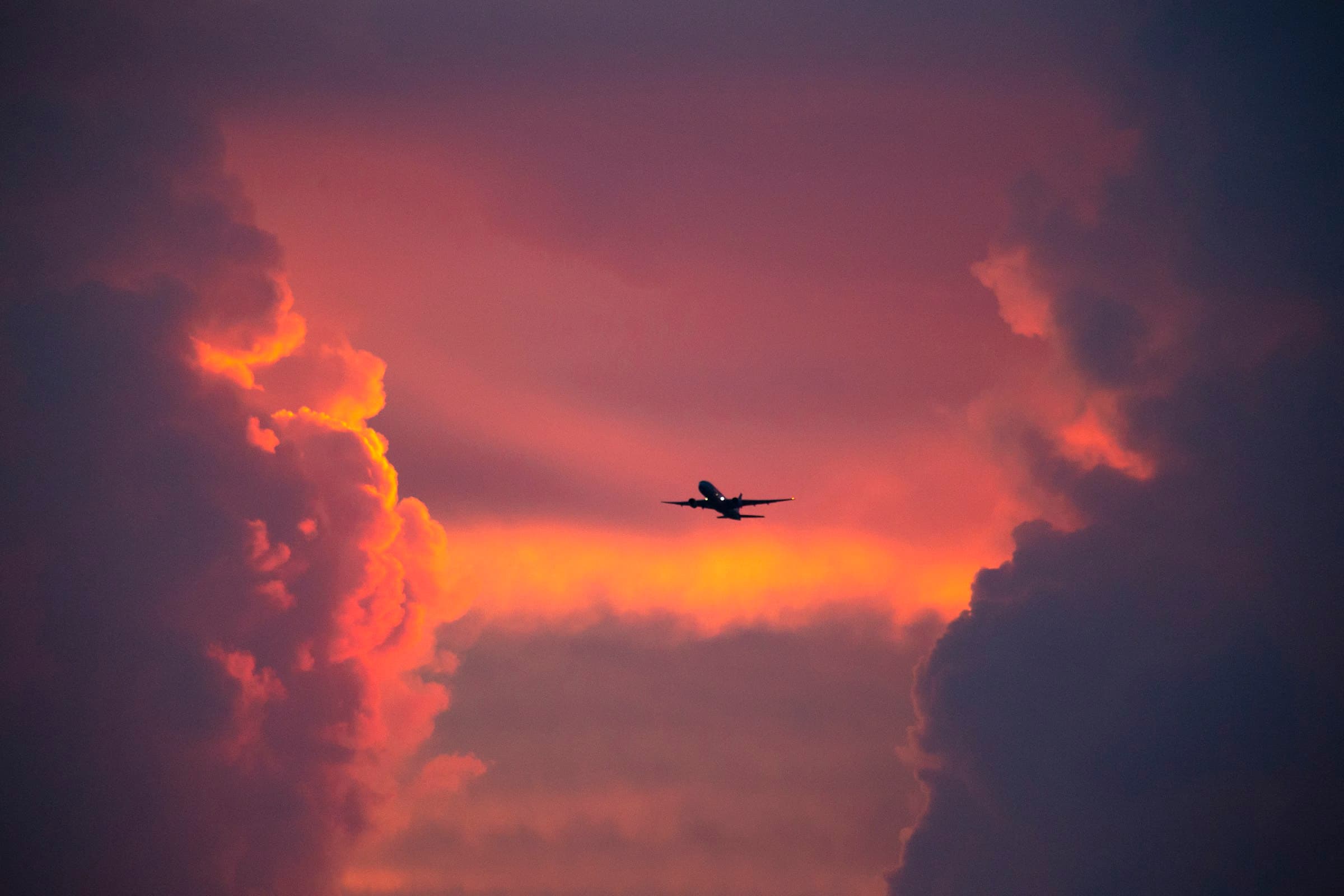 Commercial airplane flying toward the right across a dramatic sunset sky